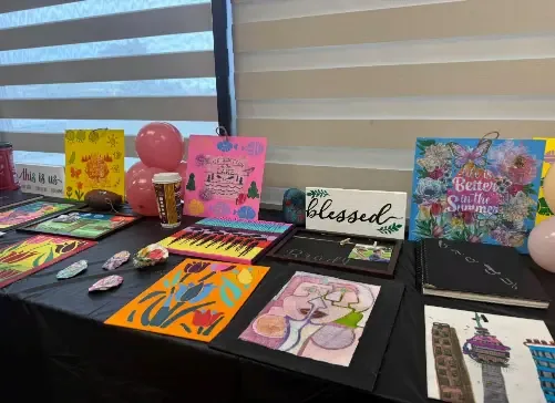 A table display of colourful paintings and crafts created by Resourceful Futures clients