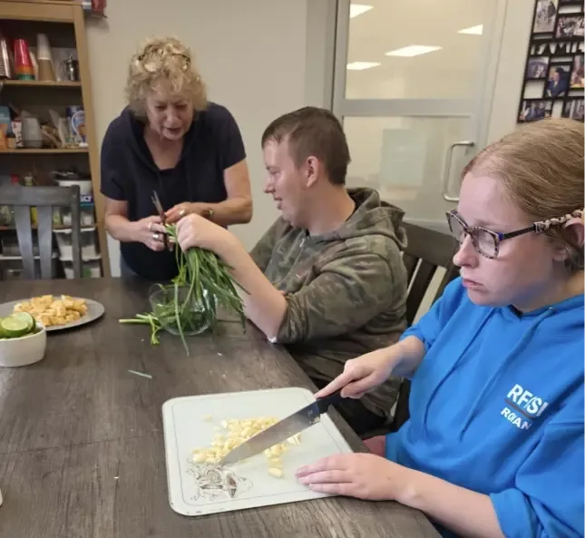 A client chopping vegetables with staff support during cooking class